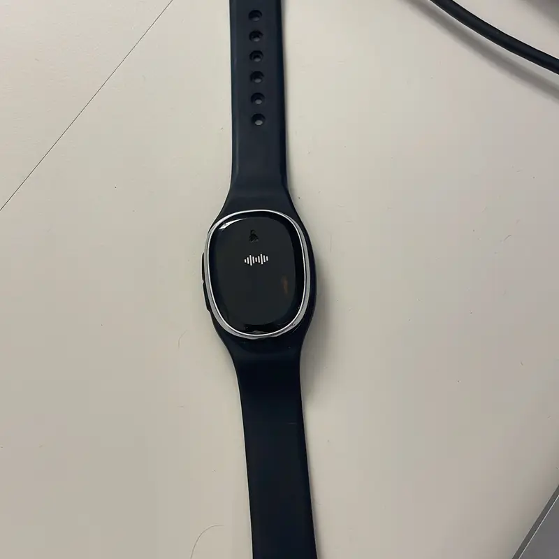 A black fitness band with a rounded module, lying on a desk beside its cable.