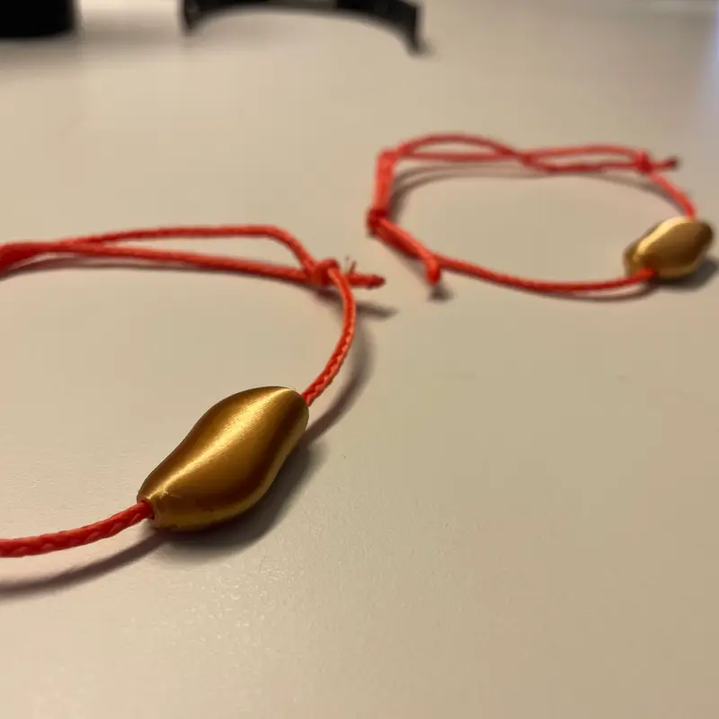 Two bracelets on red cords, each carrying a brushed gold pebble, on a desk.