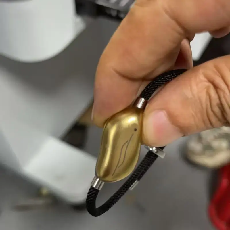 A hand holding a gold pebble on a black cord at a workbench.