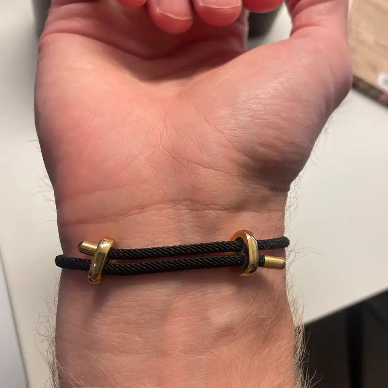 A wrist wearing a dark cord bracelet with gold end fittings, next to a wooden bead bracelet.