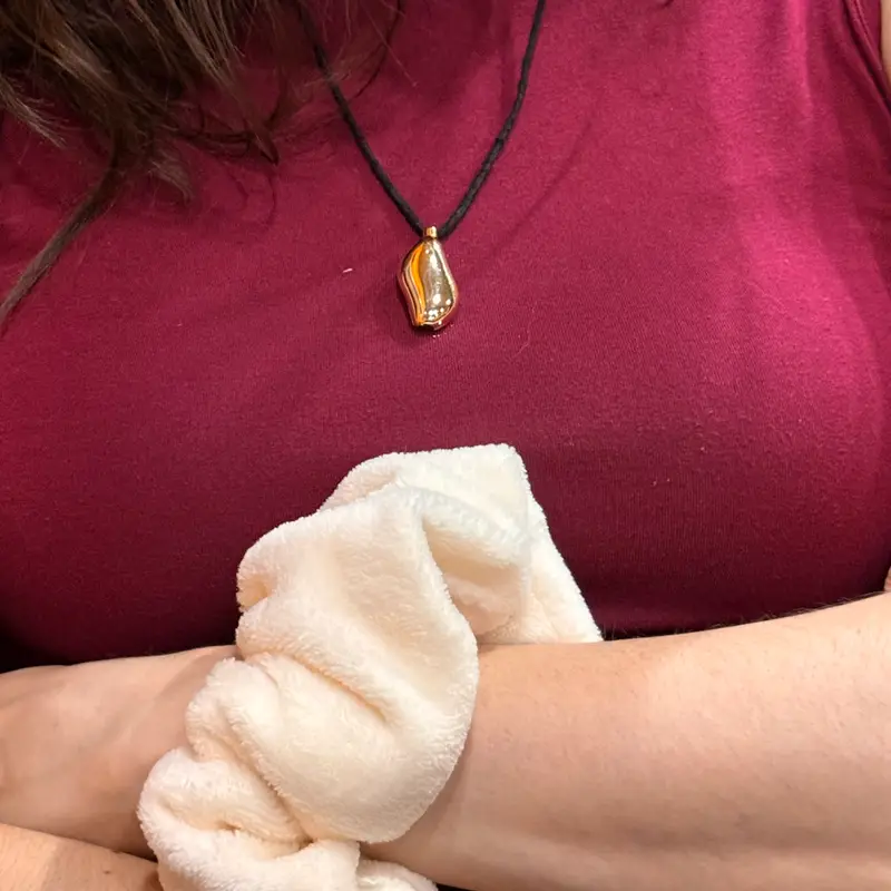 The pebble worn as a pendant on a black cord over a magenta top, with a band on the wrist below.