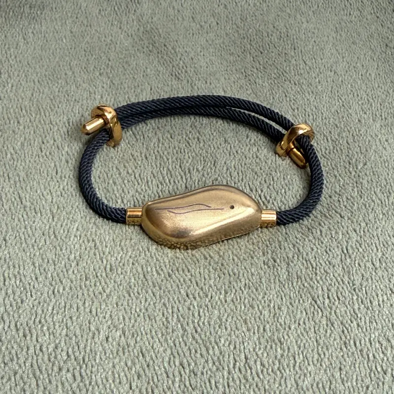 The finished Sou Band: a navy cord with gold fittings and a brushed gold pebble, on grey fabric.