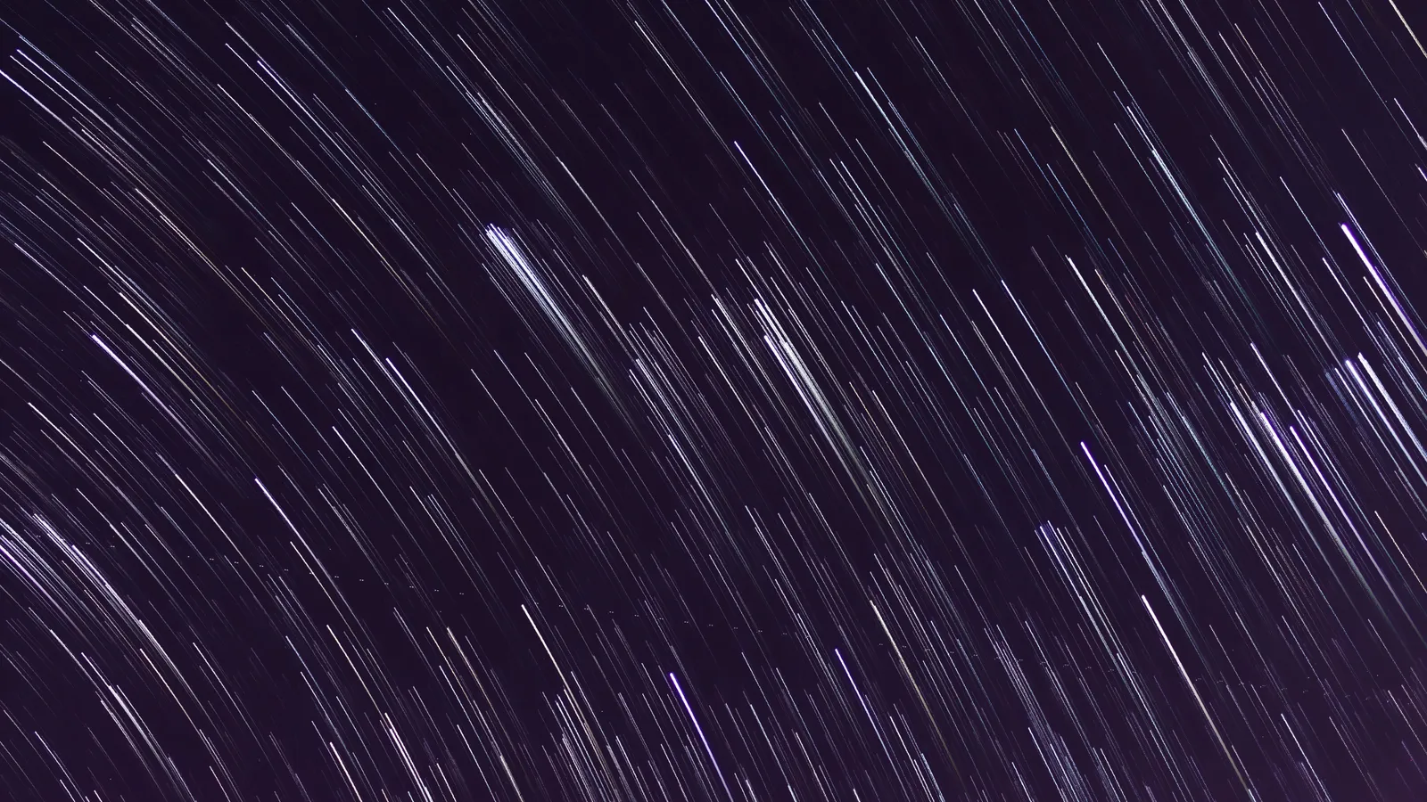 An abstract long-exposure photograph of a night sky, the stars drawn into fine parallel streaks of white and pale violet across deep purple-black.
