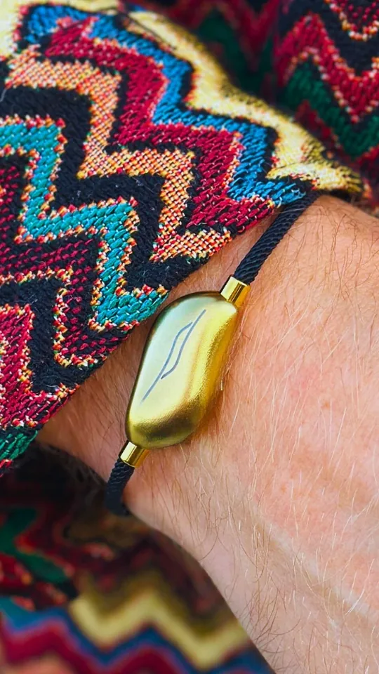 A wrist wearing the Sou band beside a colourful woven bracelet